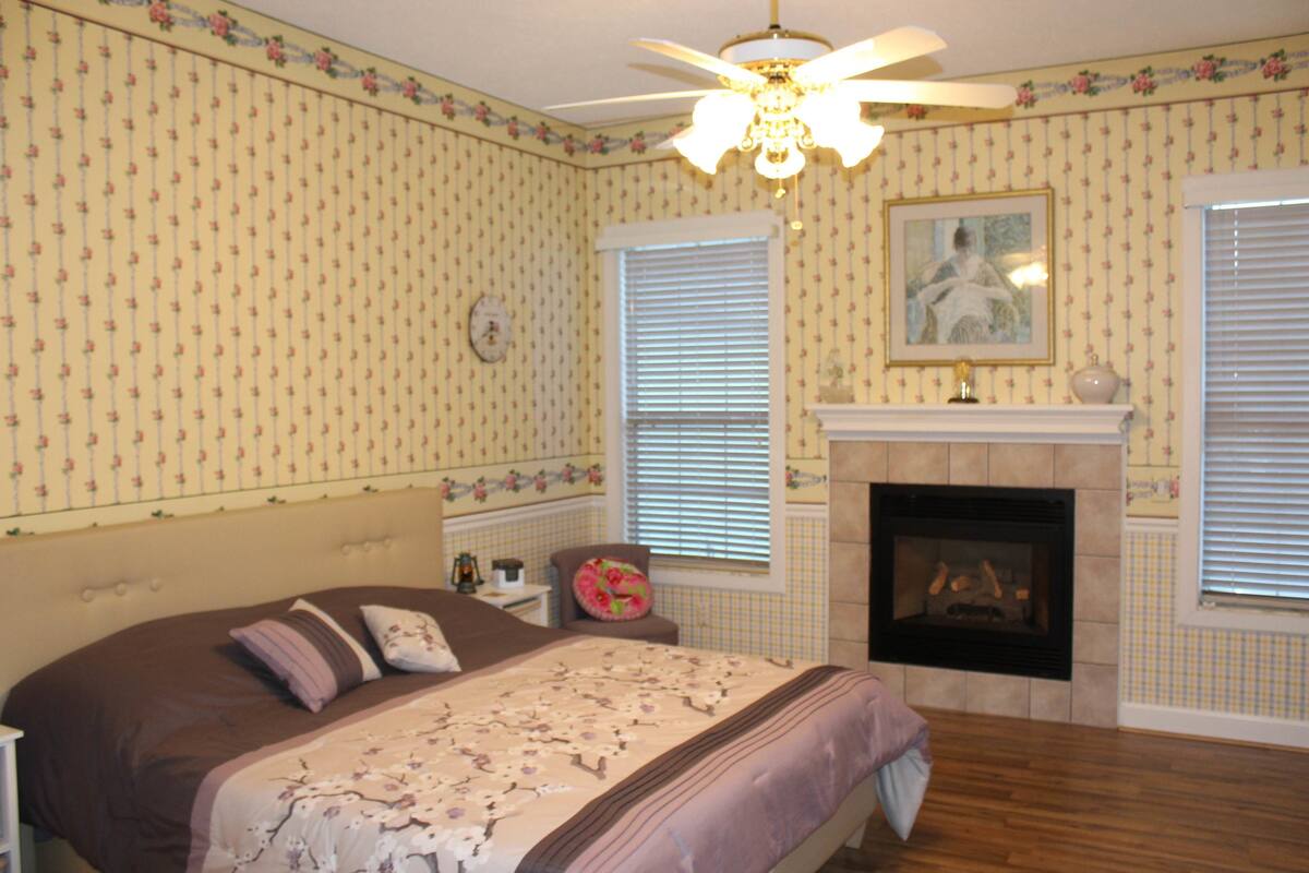 Un dormitorio con cama, chimenea, ventilador de techo y papel tapiz floral.