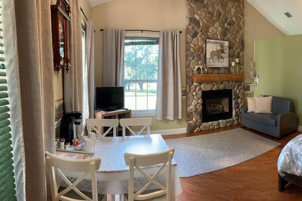 Un dormitorio acogedor con cama, chimenea, rincón comedor con mesa y sillas, y vistas al exterior.