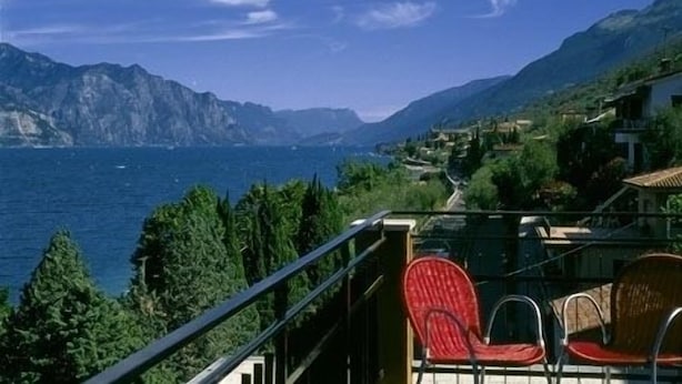 Un balcon avec des chaises rouges donnant sur un paysage côtier, avec des montagnes et la mer.