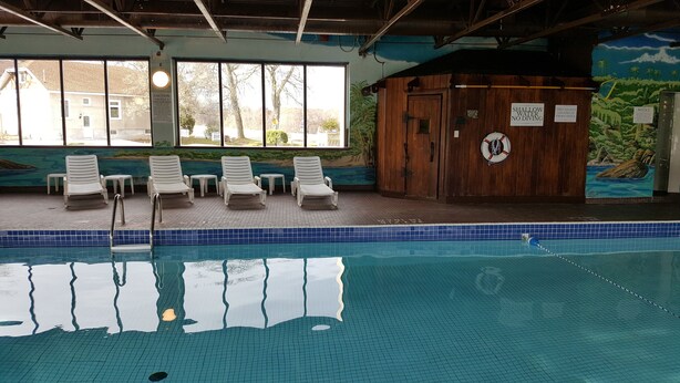 An indoor swimming pool with clear water, lounge chairs, and safety signs. - River Rapids Inn (Niagara Falls)