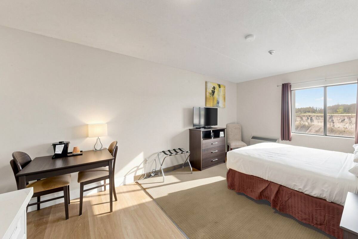 Habitación de hotel con cama, escritorio, silla, televisor y vistas al exterior.