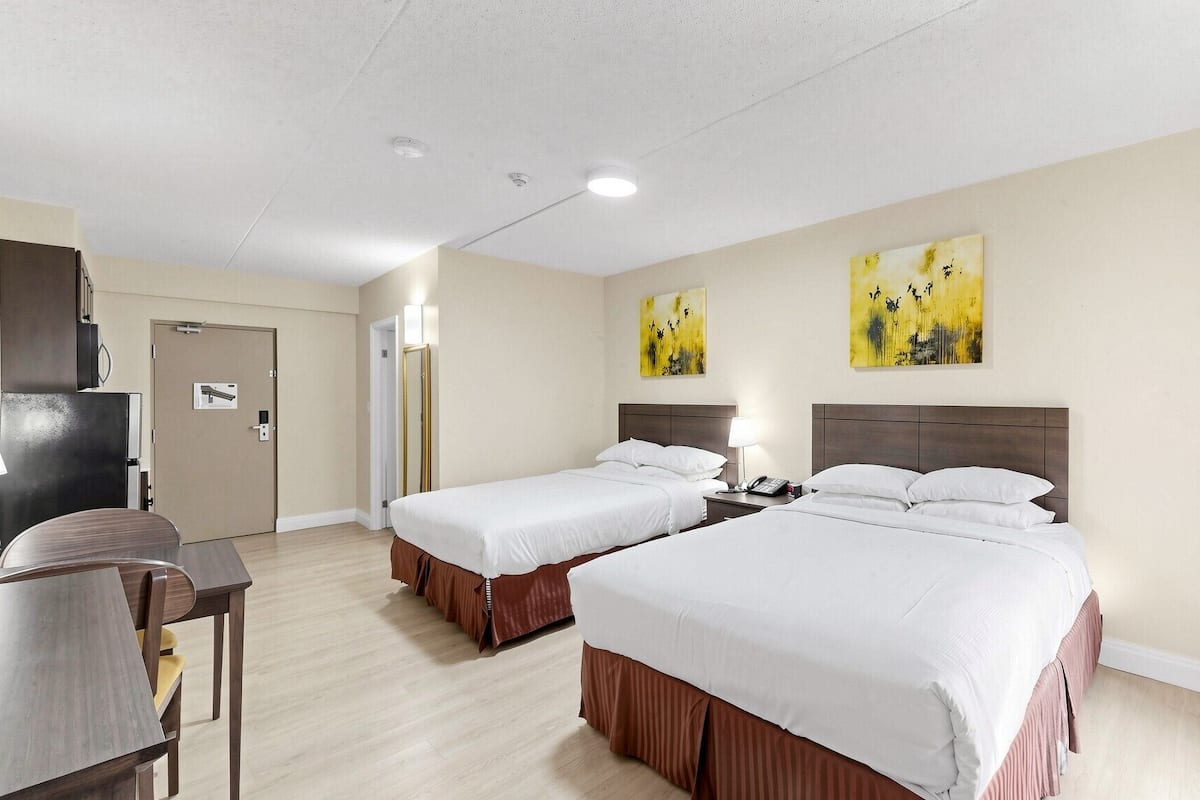 Una habitación de hotel con dos camas, un escritorio, un espejo y obras de arte en las paredes.