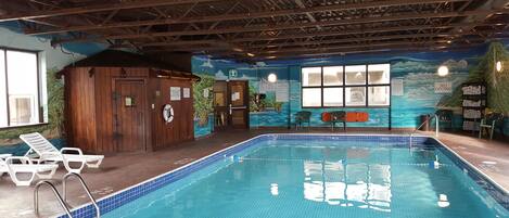 An indoor swimming pool with a mural of a beach scene, a wooden cabin, and a lifeguard station.