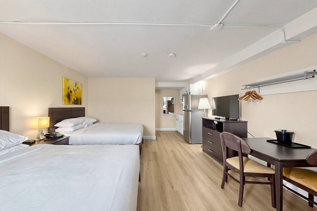Habitación de hotel con dos camas, un escritorio, una silla, un televisor, un refrigerador y un espejo.