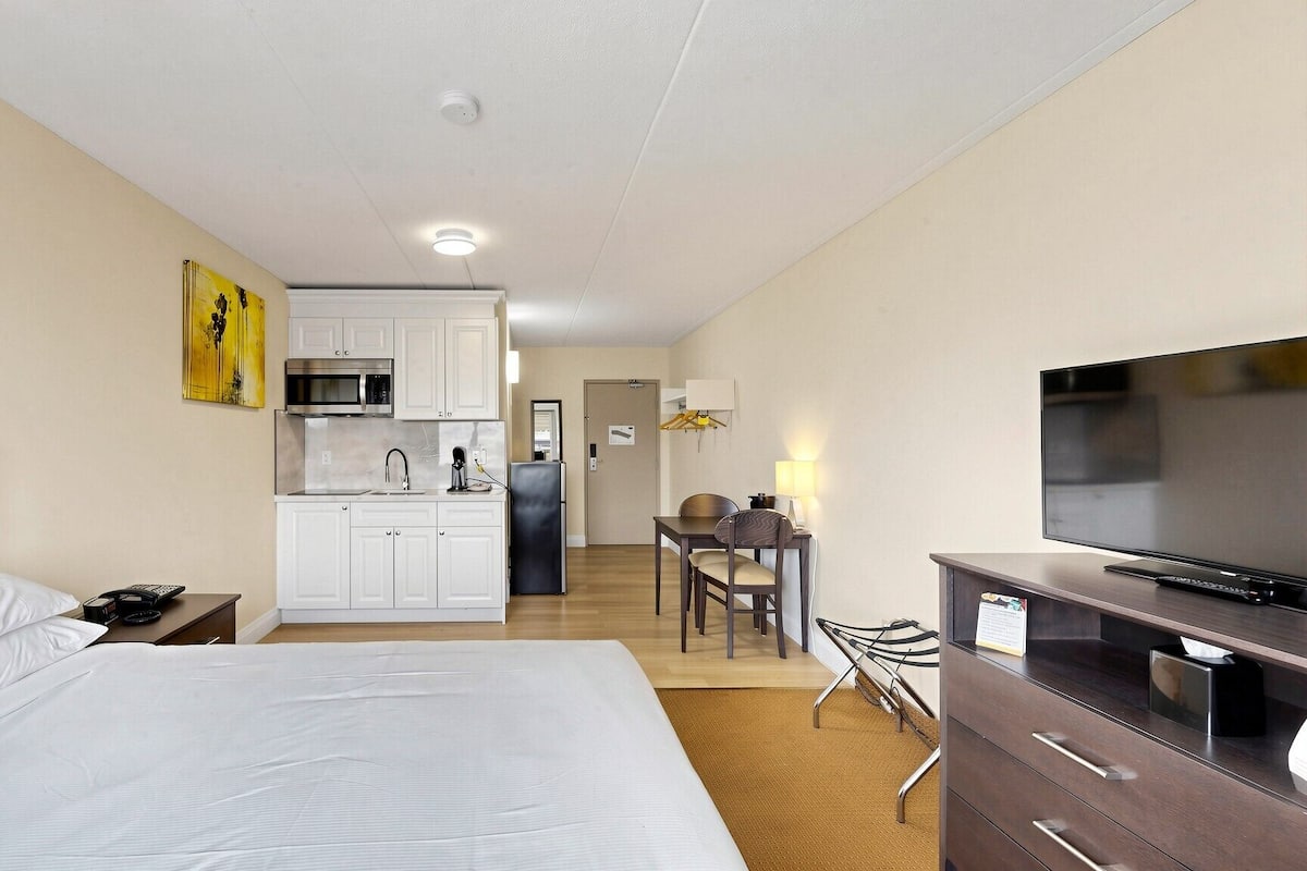 Habitación de hotel con cama, televisión, escritorio con silla, kitchenette y baño.