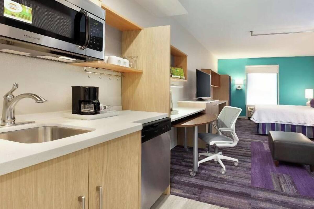 A compact hotel room with a kitchenette, a bed, a desk, and a chair.