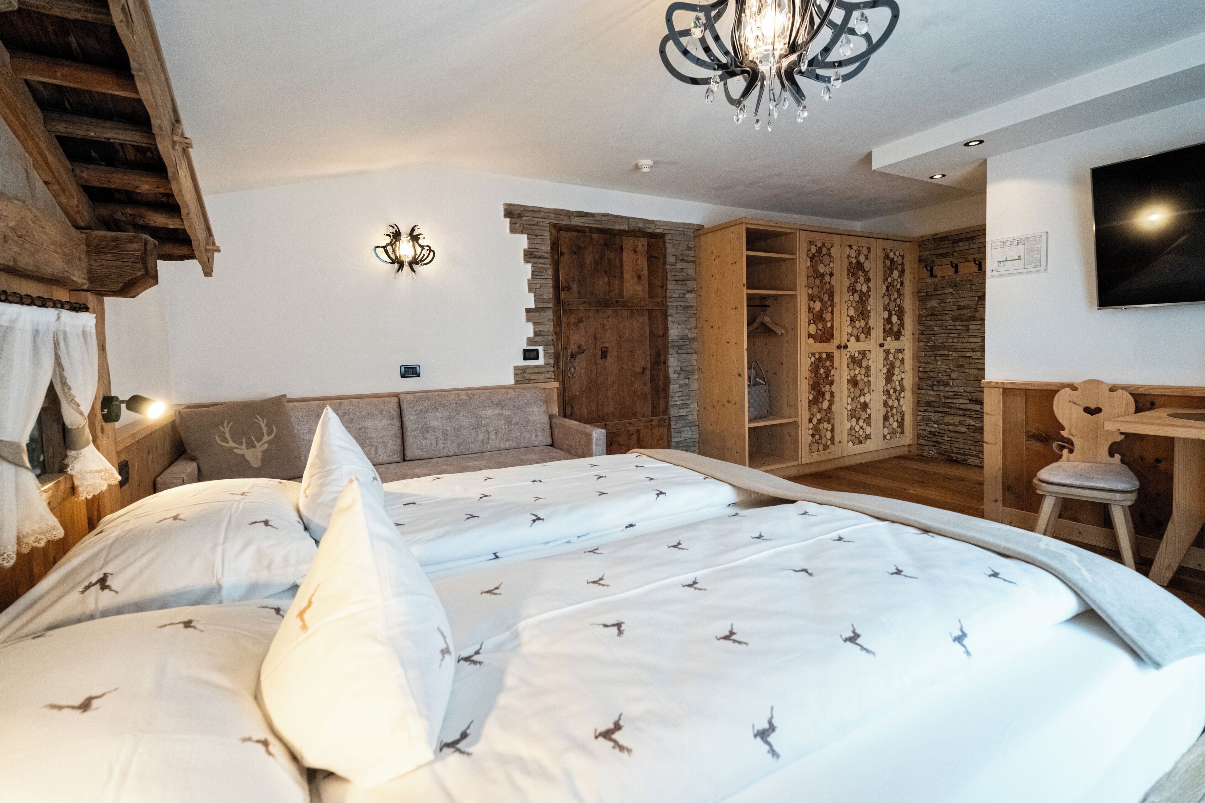 Quarto com cama grande, cabeceira de madeira, lustre, guarda-roupa e televisão.