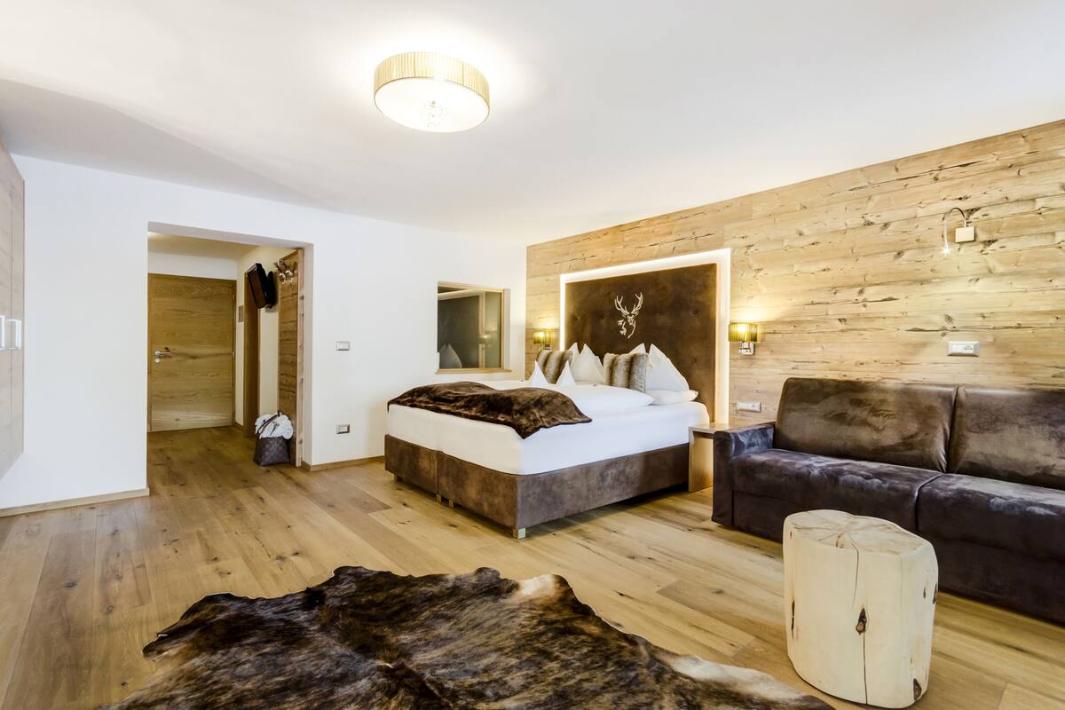 A modern bedroom with a wooden wall, a large bed, a leather sofa, and a rustic rug.