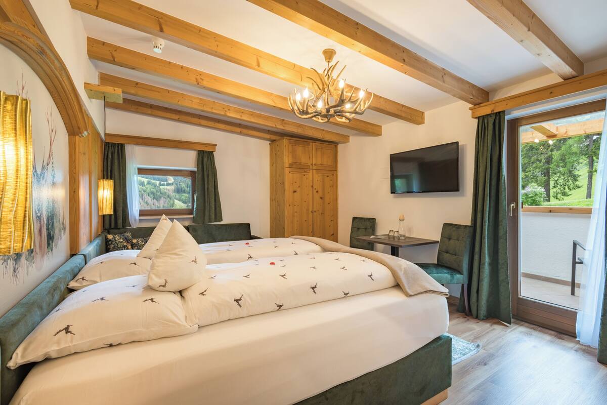 A bedroom with a large bed, a television, a desk, and a view of the outdoors.