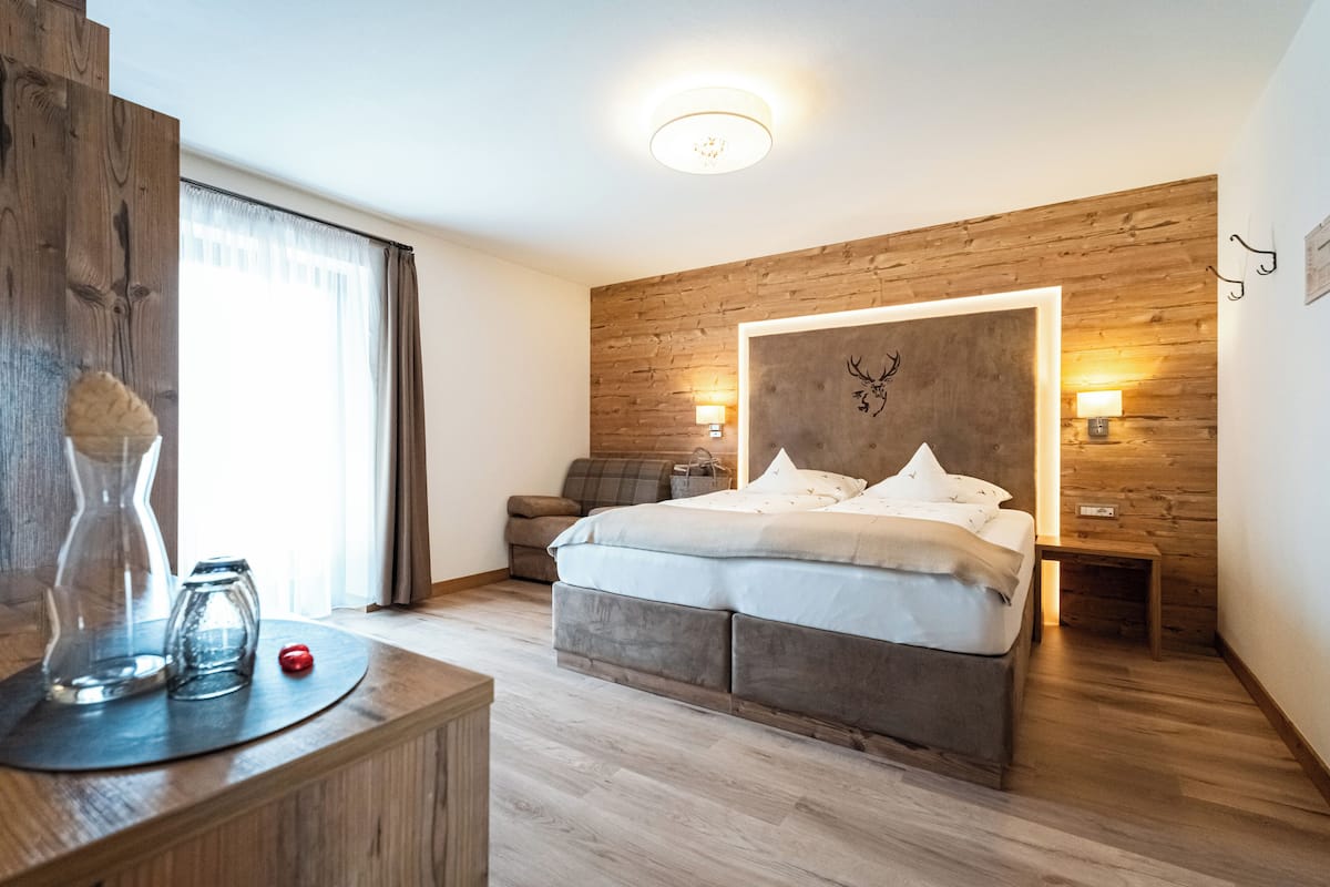 A modern bedroom with a wooden headboard, a bed with white bedding, a bedside table with a vase and a red object, and a nightstand with a lamp.
