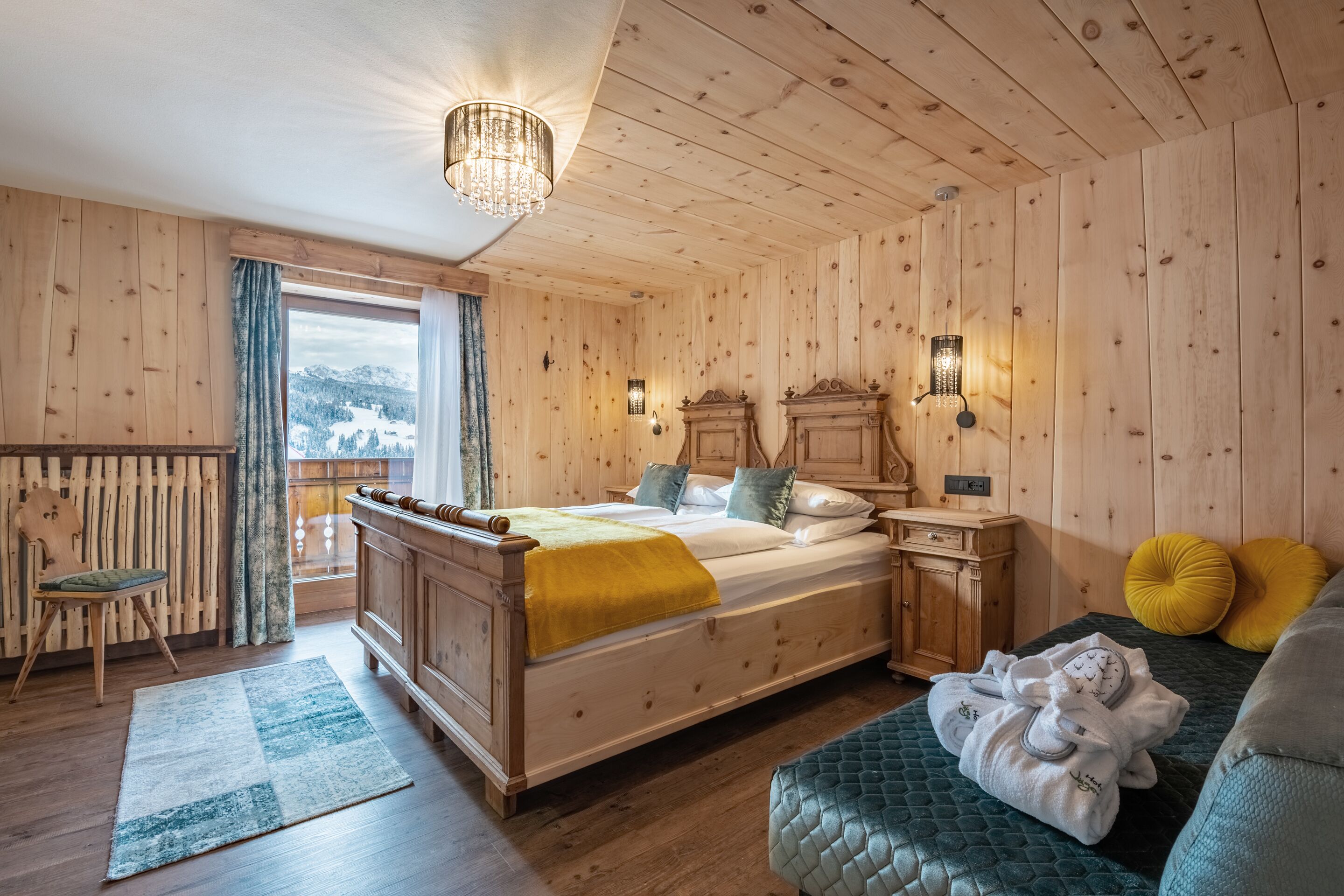 Ein Schlafzimmer mit Holzwandverkleidung, einem Bett, Nachttischen, einem Sessel und Blick ins Freie.