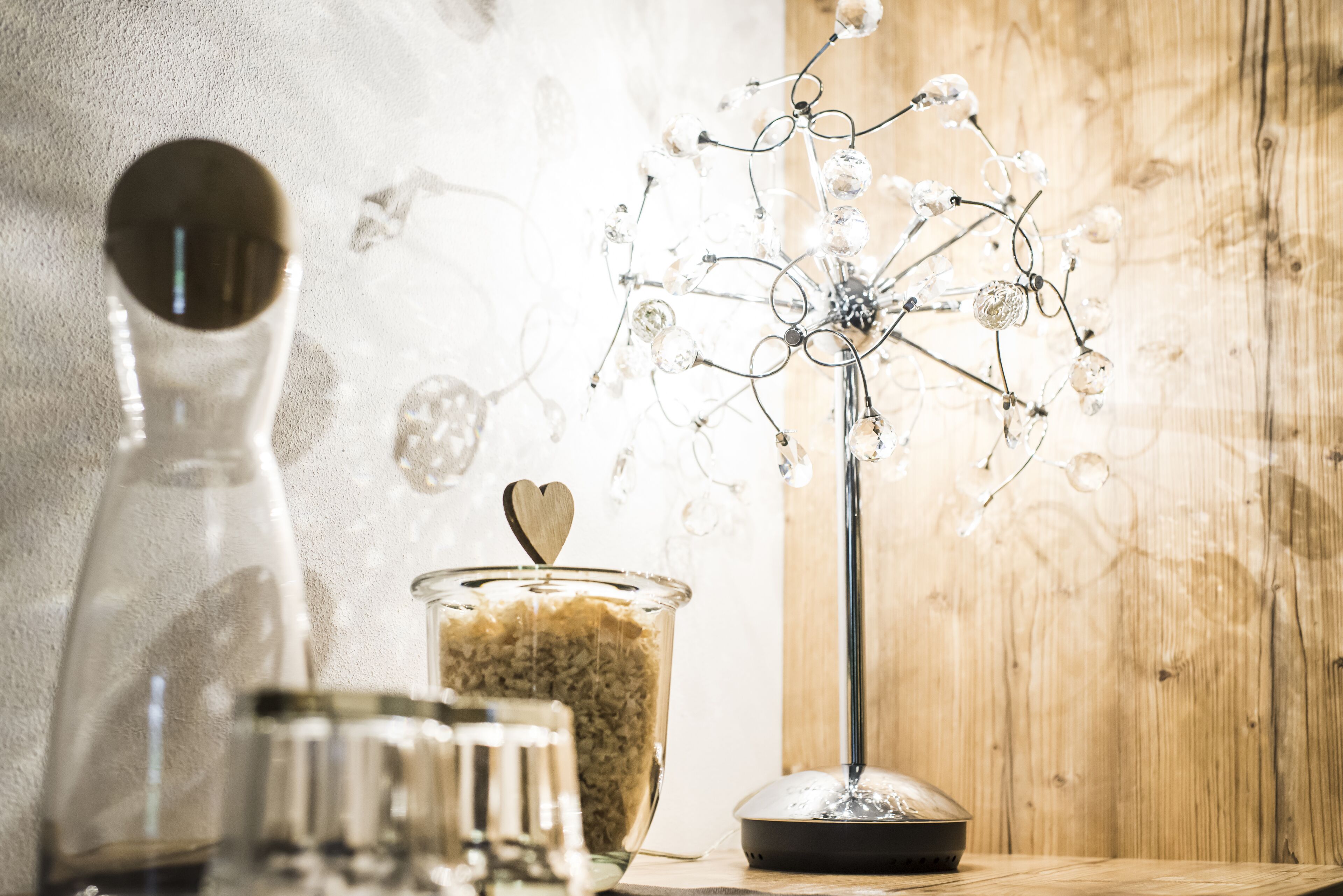 A clear glass bottle, a glass jar with a heart-shaped lid, and a decorative metal tree-like structure with crystal-like elements.