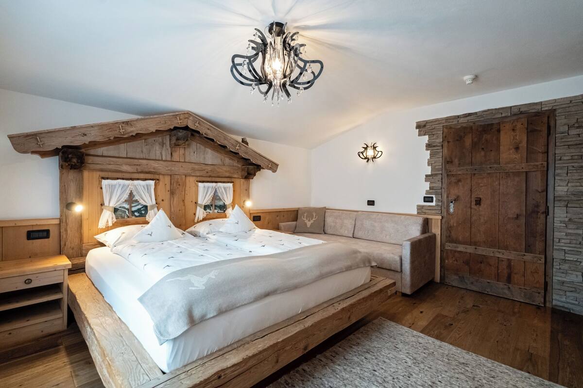 A wooden bedroom with a large bed, a bench, and a rustic ceiling design.