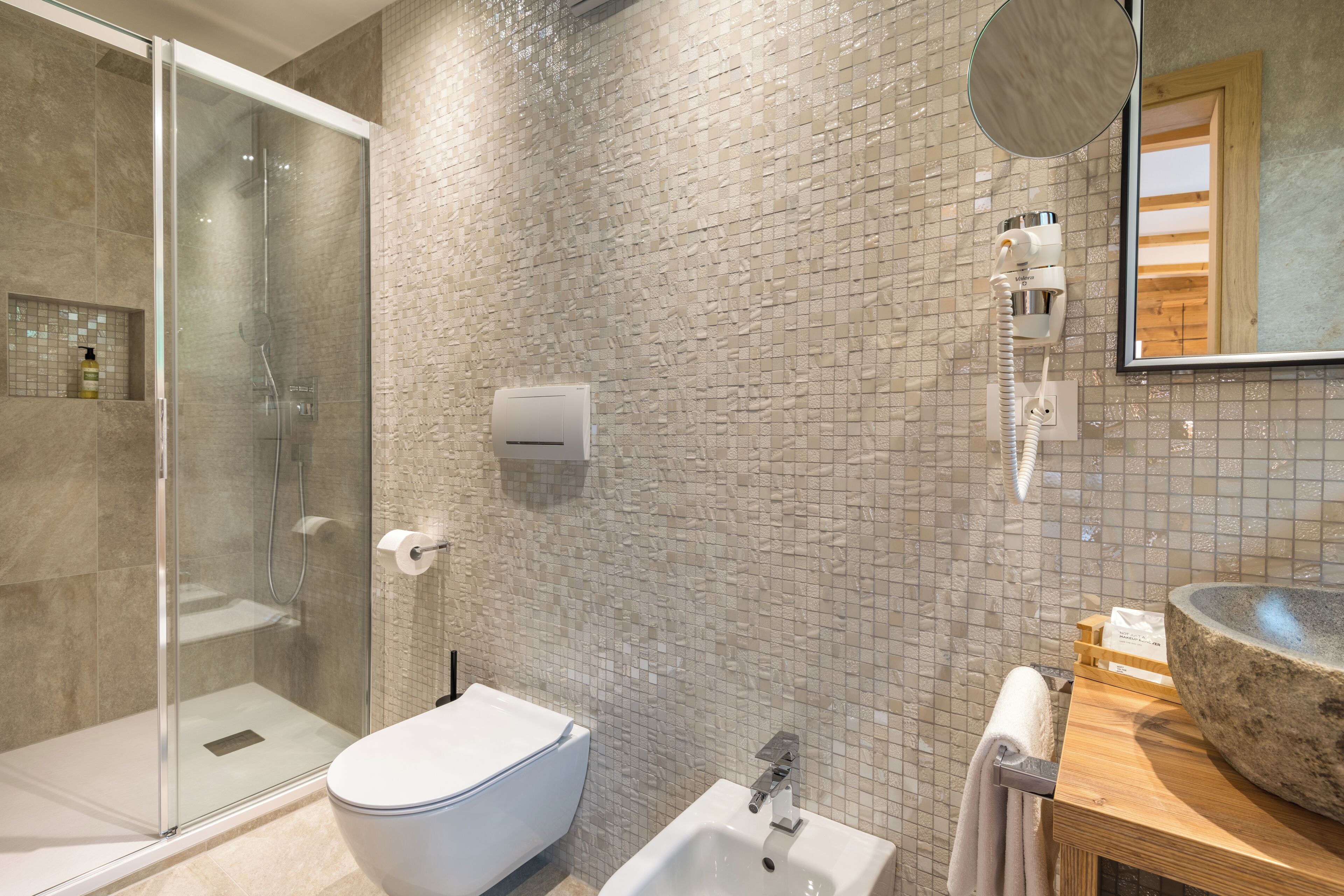 A modern bathroom with a glass shower enclosure, a white toilet, a bidet, and a large stone sink.