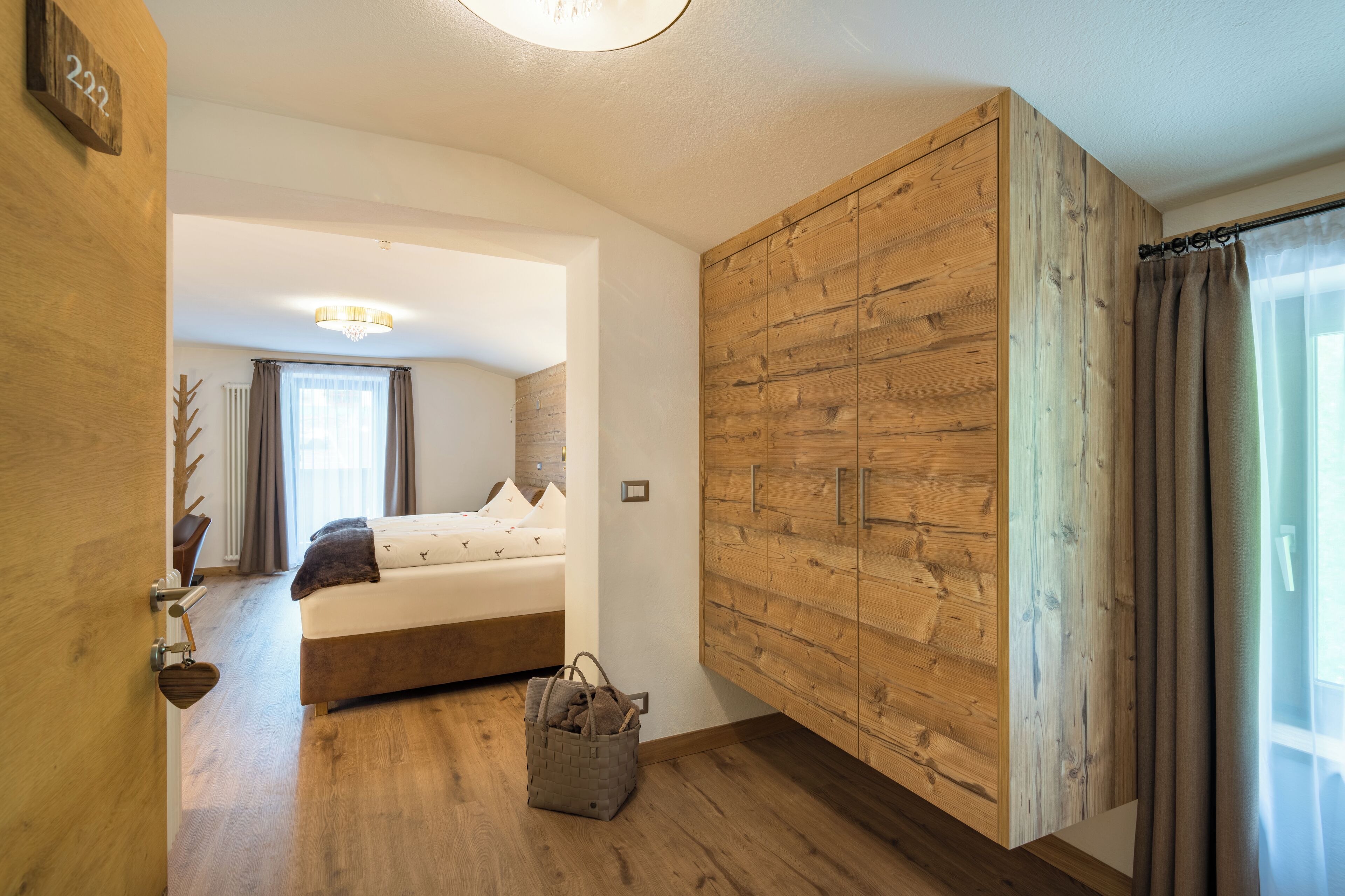 Een slaapkamer met een houten garderobe, een bed met kussens, een nachtkastje en een klein houten kistje.