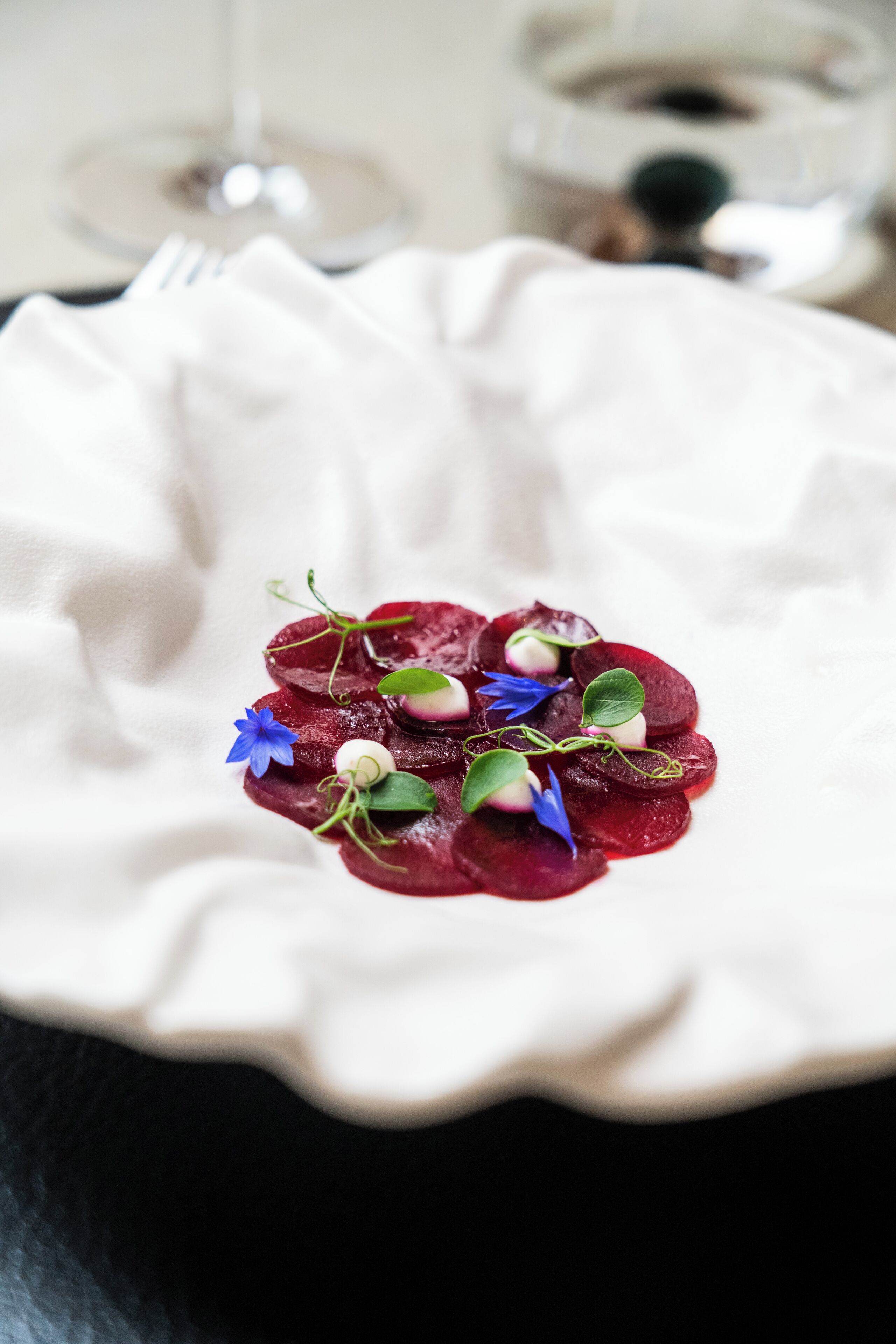 A plate of beetroot slices with flowers on a white cloth.