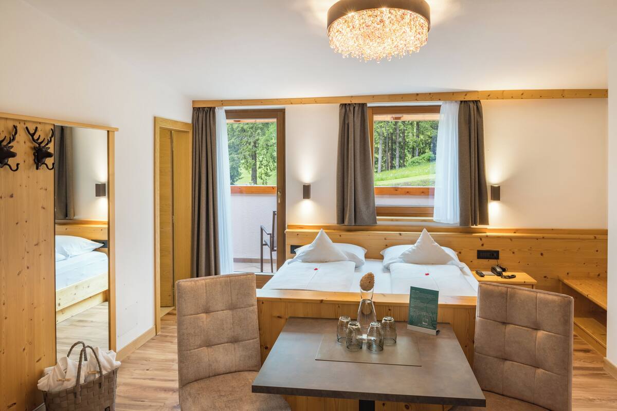 A room with a bed, a table, chairs, a chandelier, and a view of the outdoors.