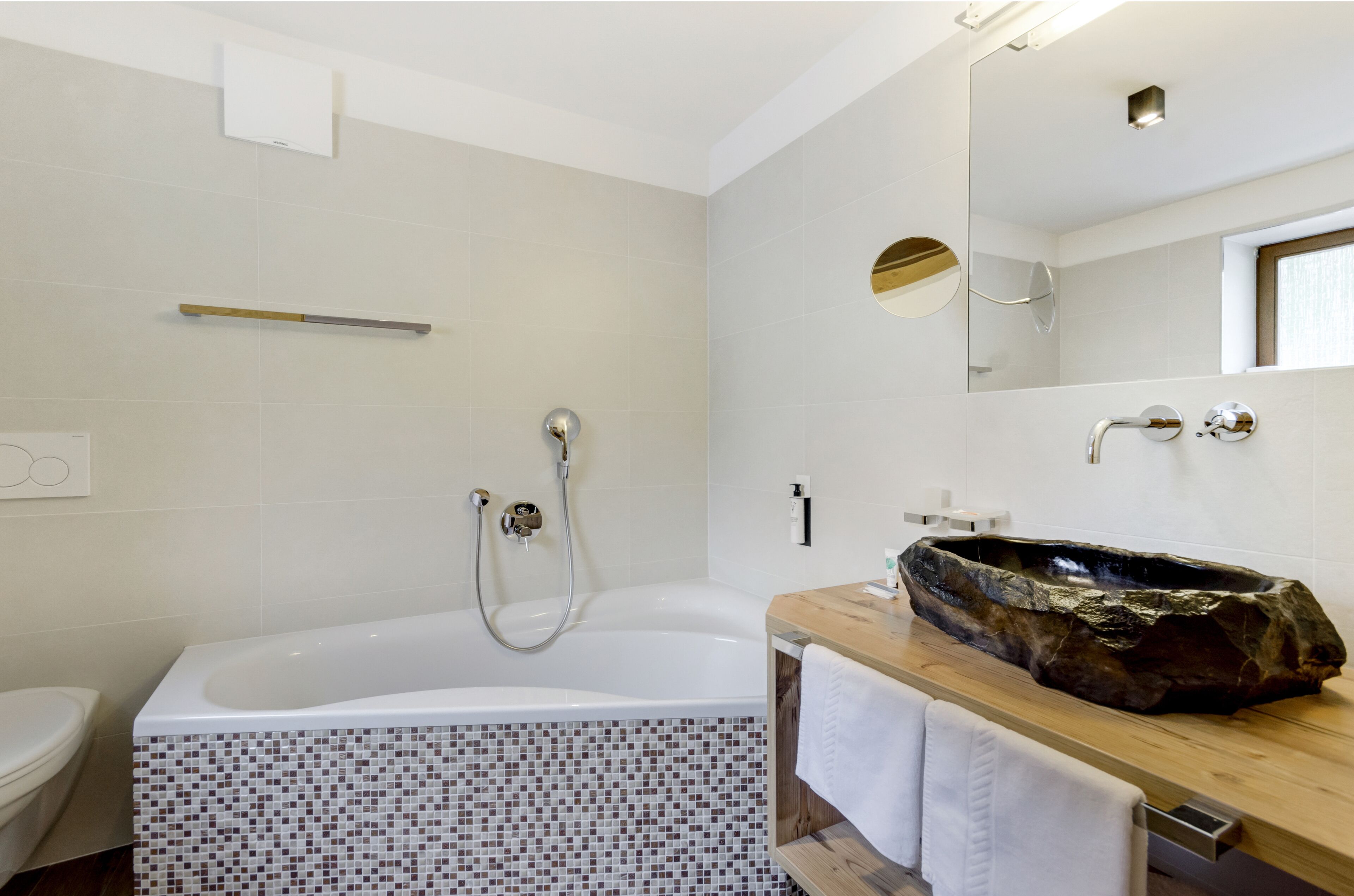 Un bagno moderno con una grande vasca da bagno, un mobile vanitario in legno, uno specchio e una zona doccia rivestita in piastrelle.