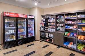 Zona de venta automática con varios refrigeradores y estantes llenos de refrigerios y bebidas.
