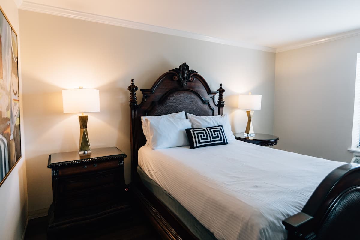 A neatly made bed with white linens and a decorative headboard, flanked by two bedside tables with lamps.