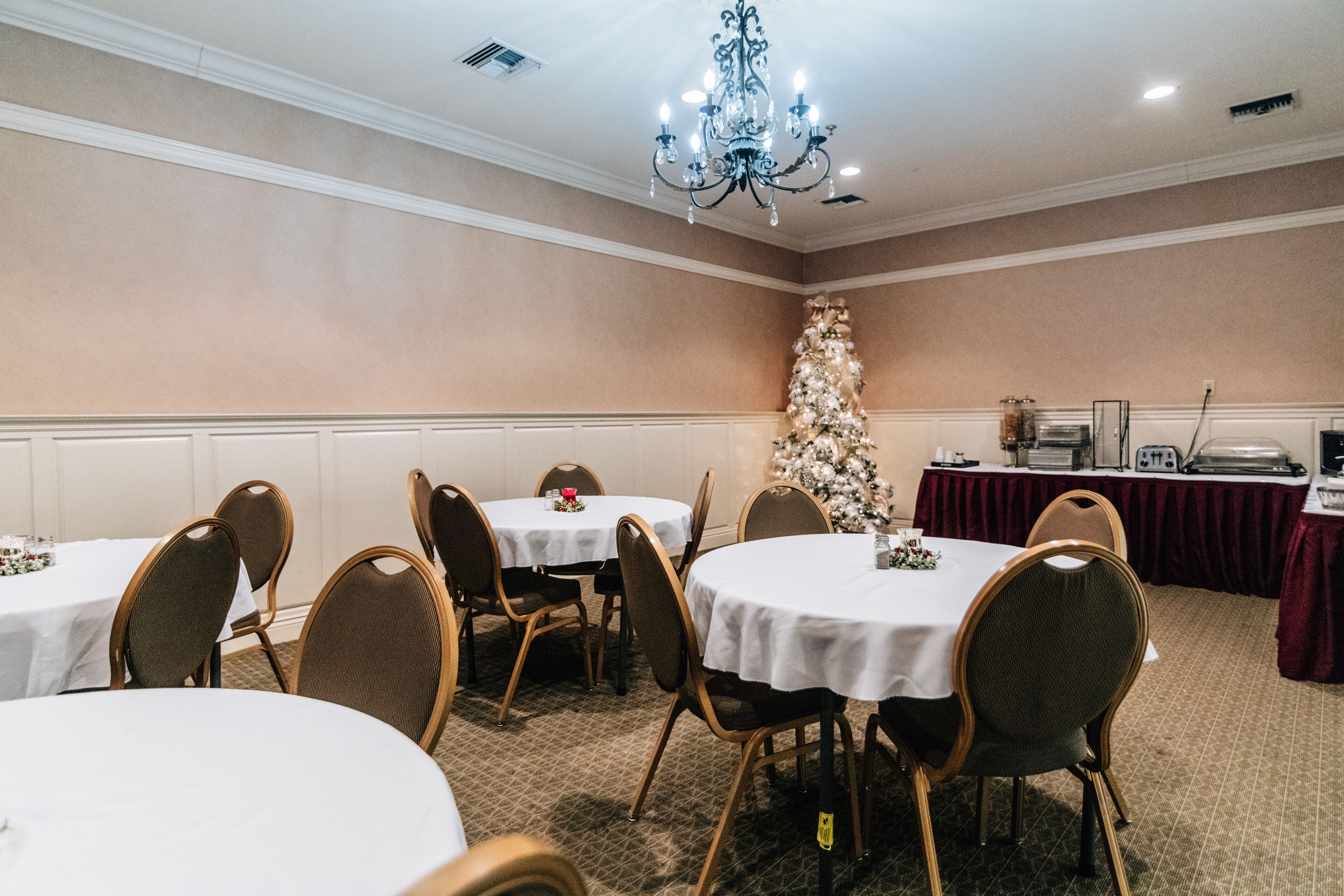A conference room with round tables and chairs, a Christmas tree, and a red tablecloth-covered table.