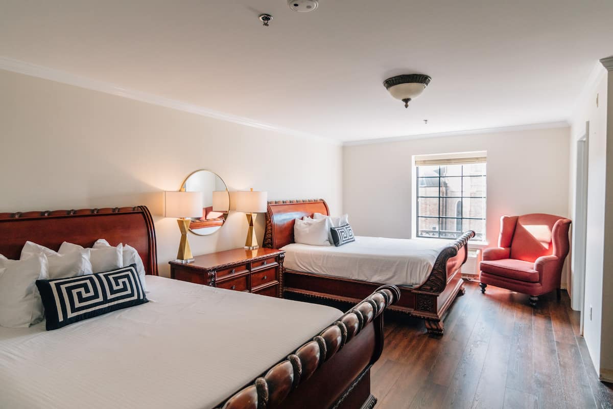 A hotel room with two beds, a red armchair, and a window with a view.