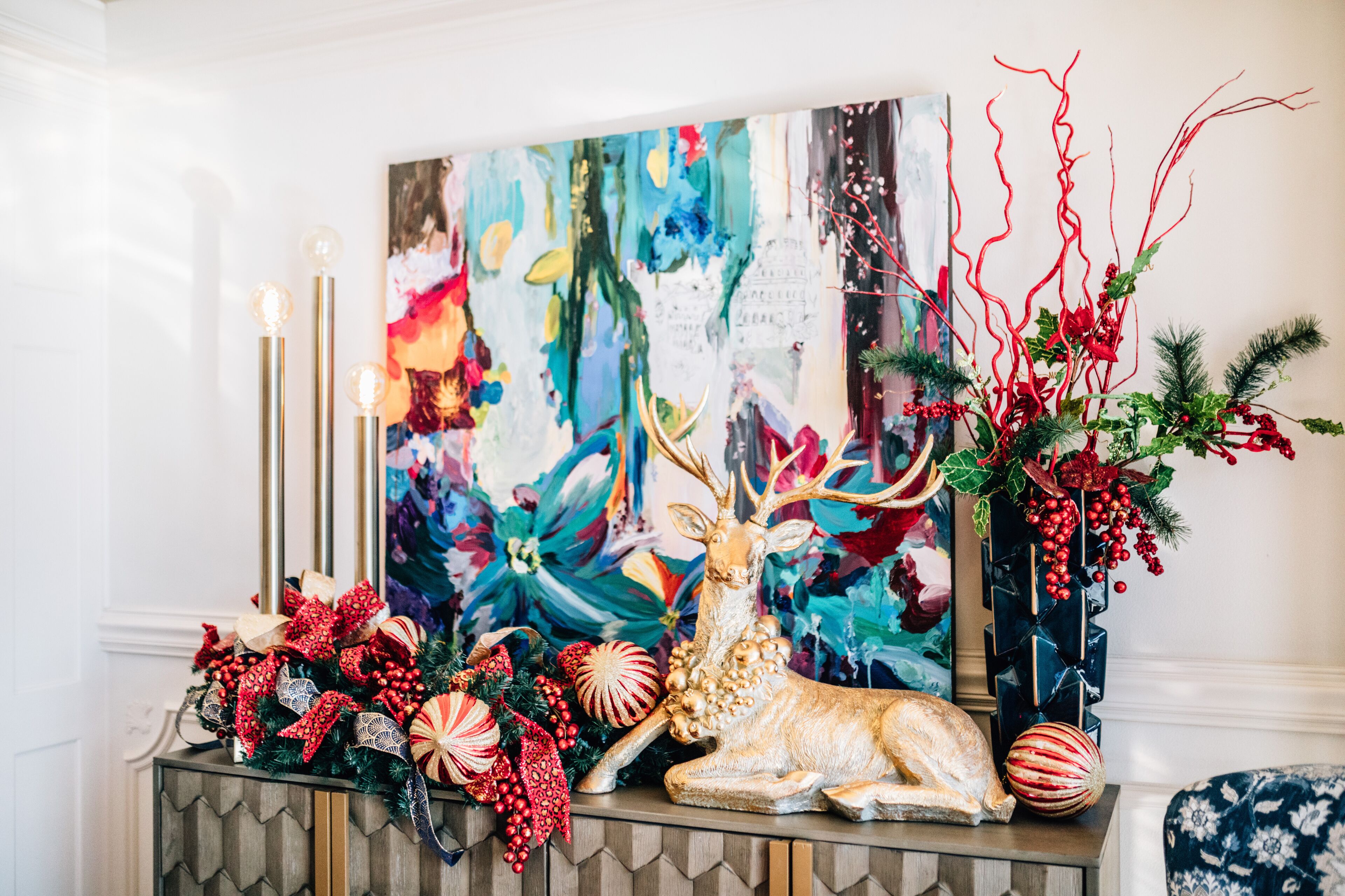 A decorated mantelpiece with a deer figurine, a painting, and various Christmas ornaments.