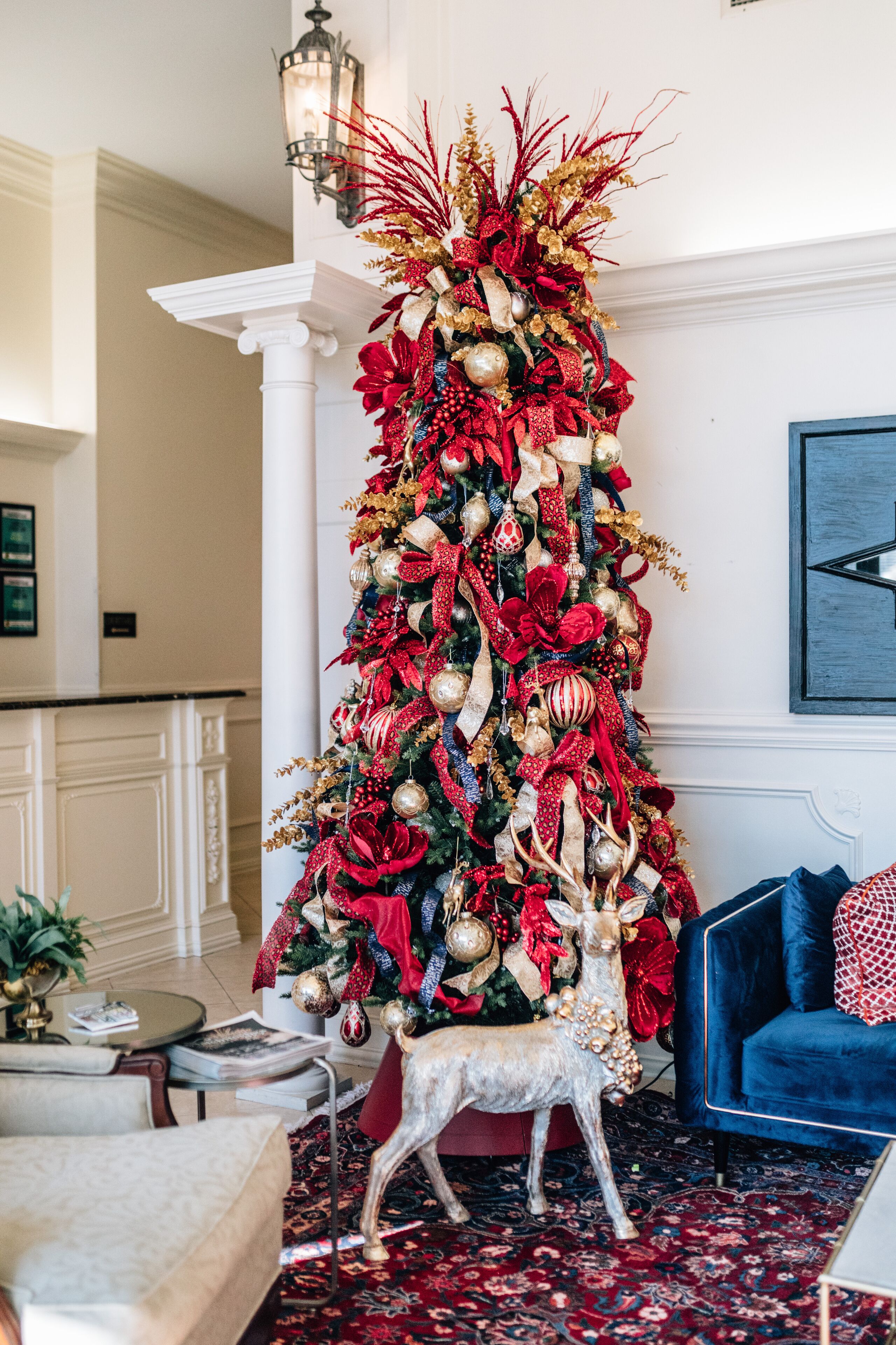A Christmas tree decorated with red and gold ornaments, ribbons, and a deer figurine.