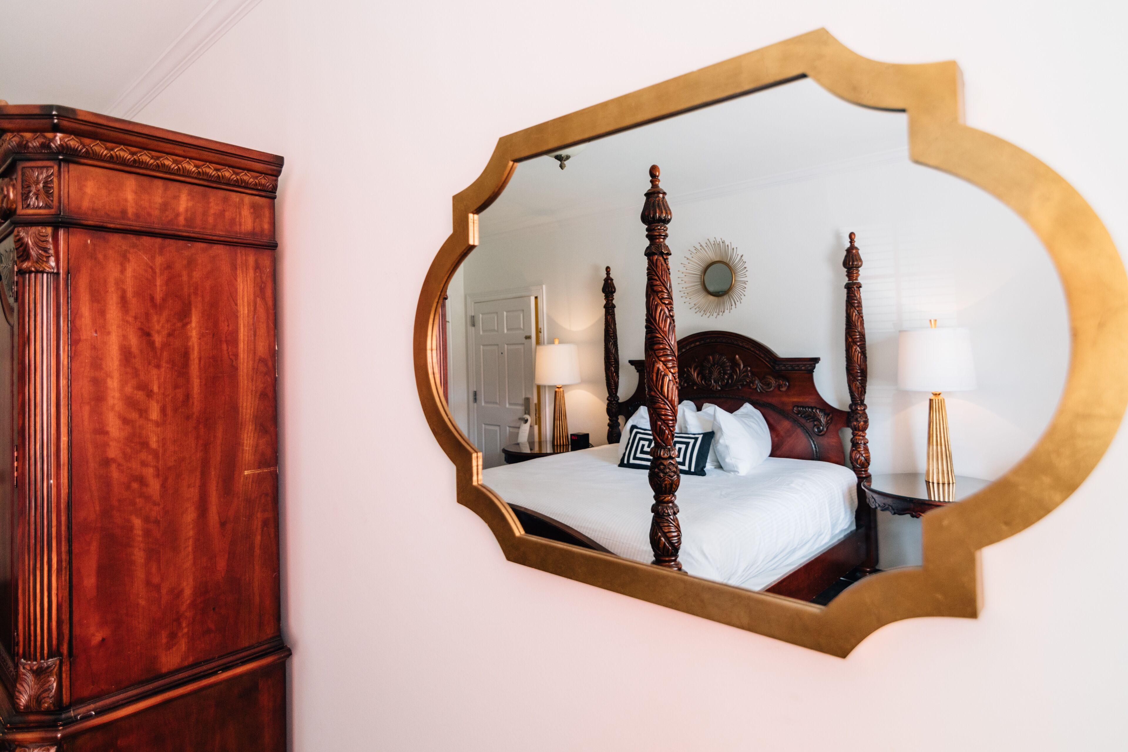 A bedroom with a four-poster bed, a large mirror, and a wooden wardrobe.