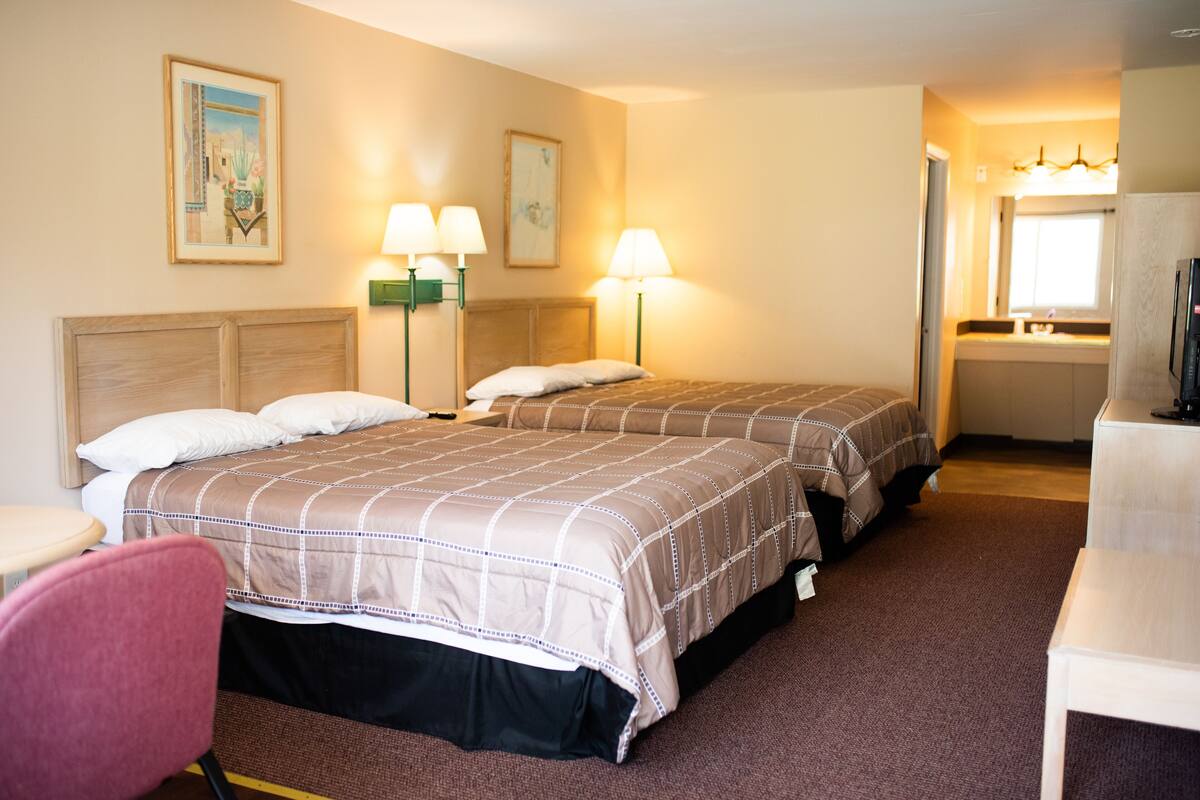 A hotel room with two beds, a desk, a chair, and a bathroom visible through an open door.