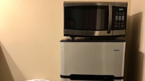 Un refrigerador Haier con un microondas encima, un bote de basura con bolsa de plástico y una pared color crema.