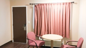Una habitación con una puerta marrón, una cortina rosa, una mesa redonda y dos sillas rosas.