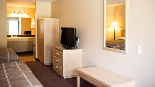 Una habitación de hotel con una cama, un escritorio, un televisor, un armario y un espejo.
