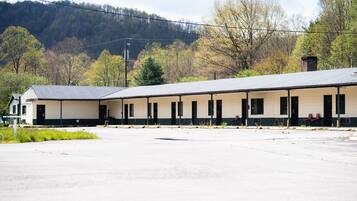 A long, single-story building with a row of rooms, a covered outdoor area, and a mountainous backdrop.