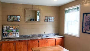 Una cocina con armarios de madera, encimera de granito, lavabo, espejo y cuadros en la pared.