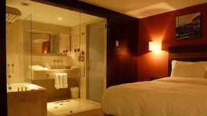 A hotel room with a glass-enclosed shower, a bed with white bedding, and a wall-mounted light fixture. - Kristoff (Maracaibo)