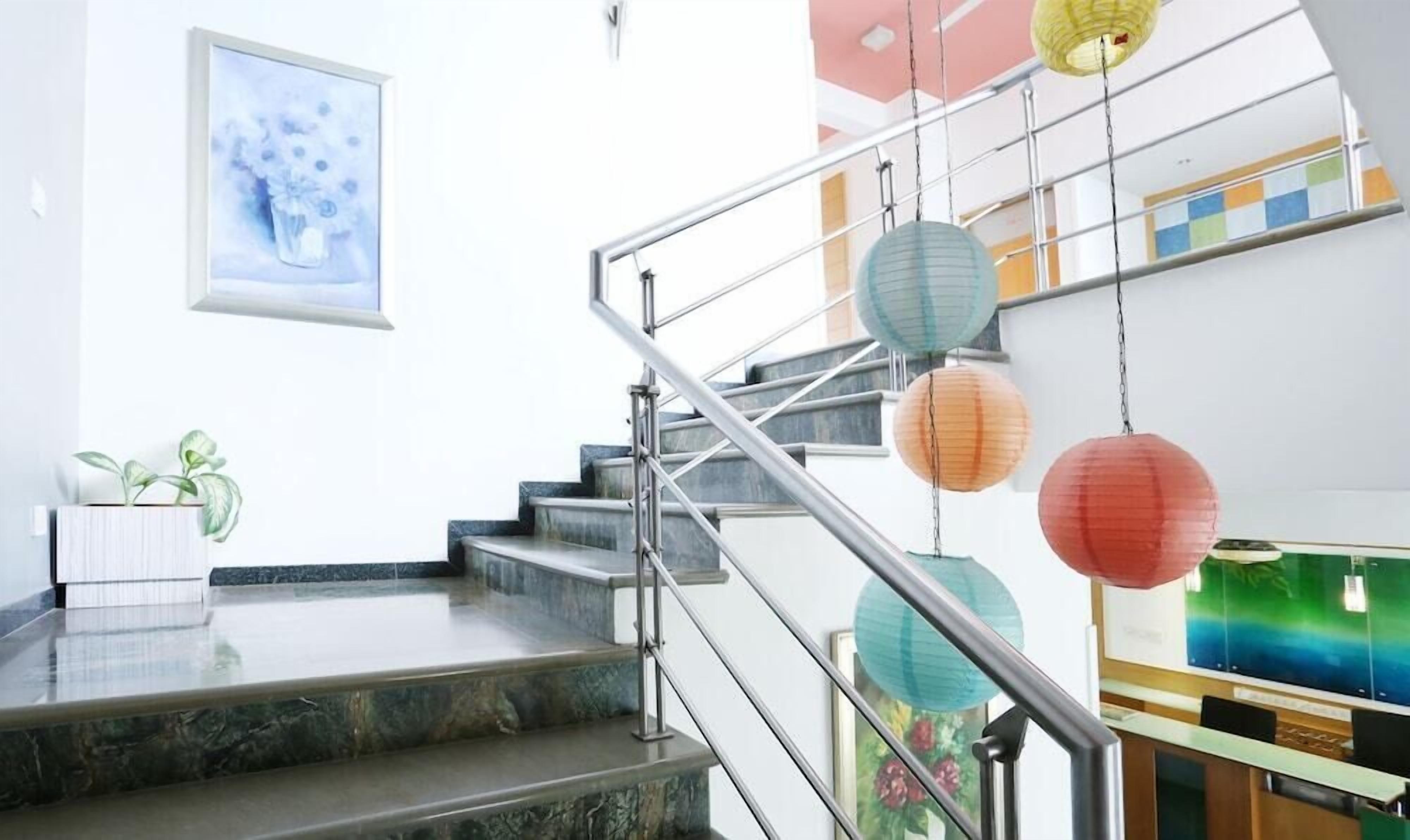A modern staircase with metal railings, a marble floor, and colorful paper lanterns.