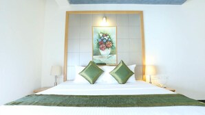 A hotel room with a large bed, two green pillows, a painting of flowers on the headboard, and two bedside lamps. - Edha Suites (Bengaluru)