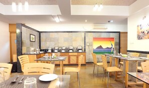 Un comedor con varias mesas y sillas, una cocina con electrodomésticos y un cuadro de un paisaje en la pared.