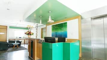 A reception area with a green accent wall, a reception desk, a seating area with a sofa and a small table, and a large window with a view of the sky.