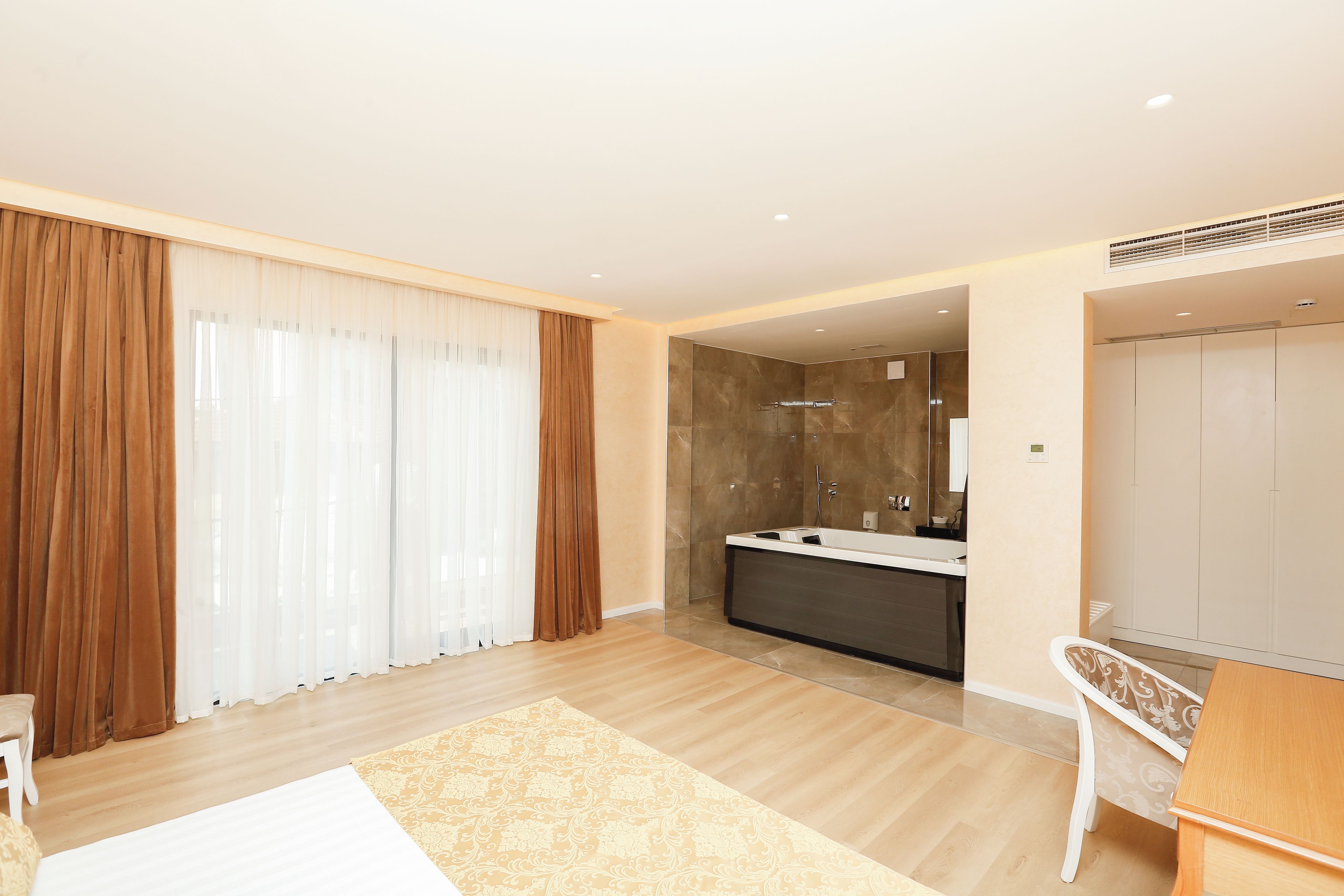 A modern hotel room with a large window, a bathtub, and a wooden floor.