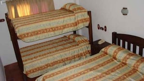 Ein Etagenbett mit gemusterten Betttextilien in einem Zimmer mit weißen Wänden, einem kleinen Tisch und einem fenster mit Vorhängen.