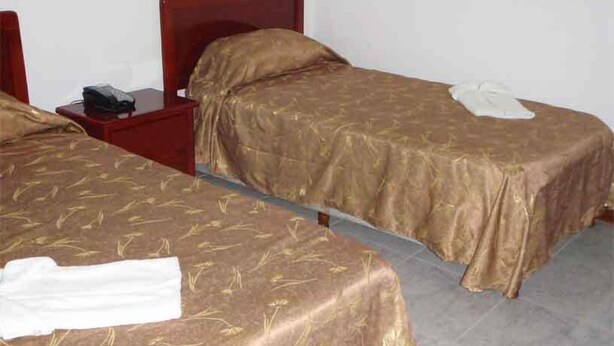 Zwei Einzelbetten mit Holz Kopfteilen, ein Nachttisch mit Telefon und ein weißes Handtuch auf einem Bett.