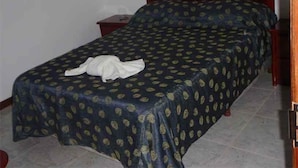 Ein Einzelbett mit dunkler, gemusterter Bettdecke und einem weißen Handtuch darauf.