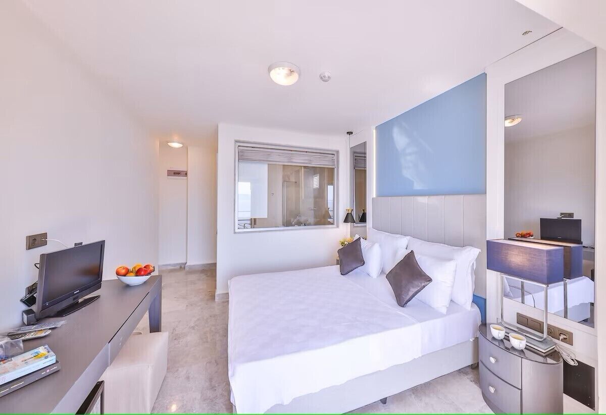 Et moderne hotelværelse med en stor seng, et fladskærms-tv, et skrivebord med en frugtskål og et spejl.