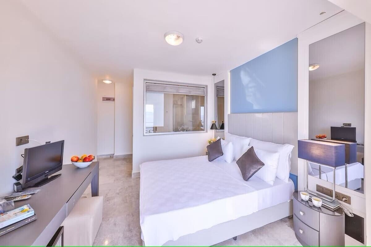 Et moderne hotelværelse med en stor seng, et fladskærms-tv, et skrivebord med en frugtskål og et spejl.