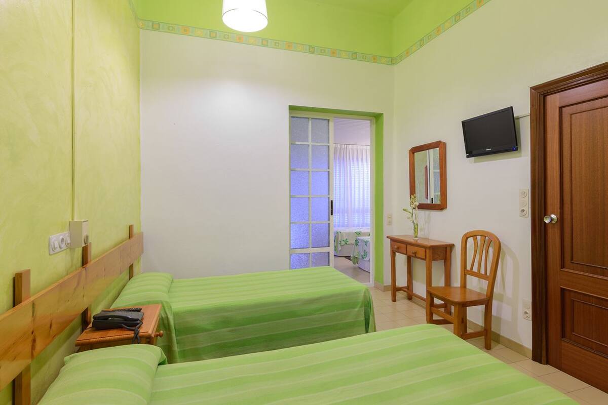 Habitación de hotel con dos camas, un escritorio, una silla, un televisor y una puerta.