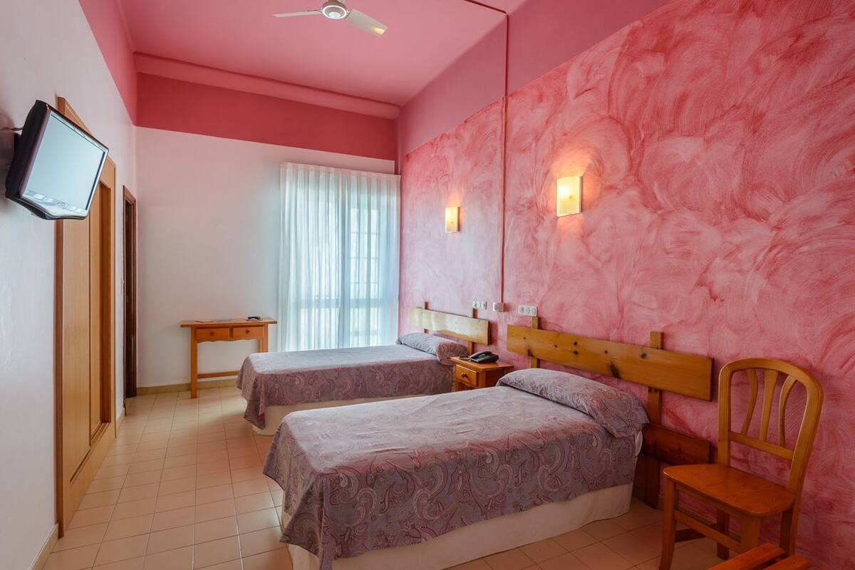 Una habitación con dos camas, un escritorio, una silla, un televisor y una ventana con cortinas.