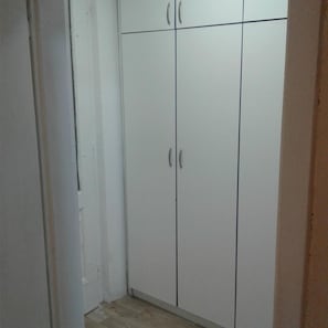 A white wardrobe with two doors and a handle, located in a room with a tiled floor. - Kamelija (Tivat)
