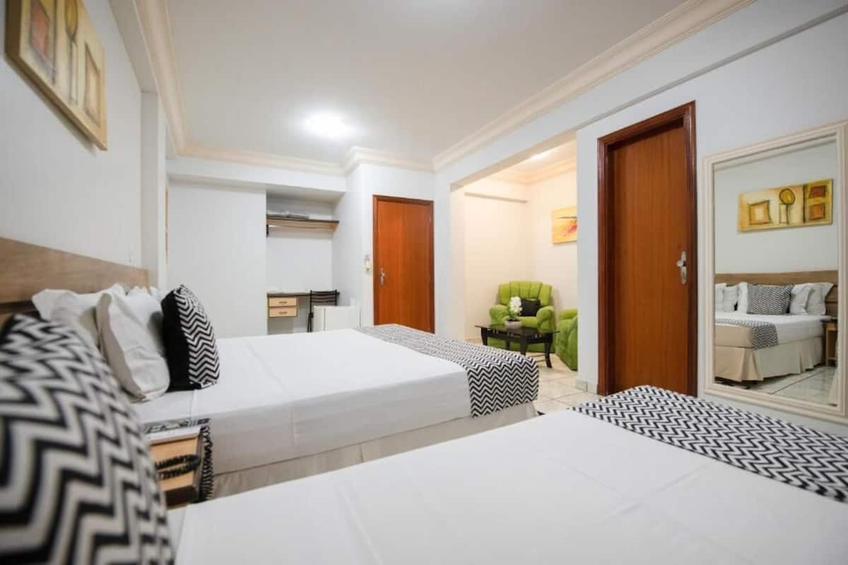 Una habitación de hotel con dos camas, un sillón verde, una mesita y un espejo.